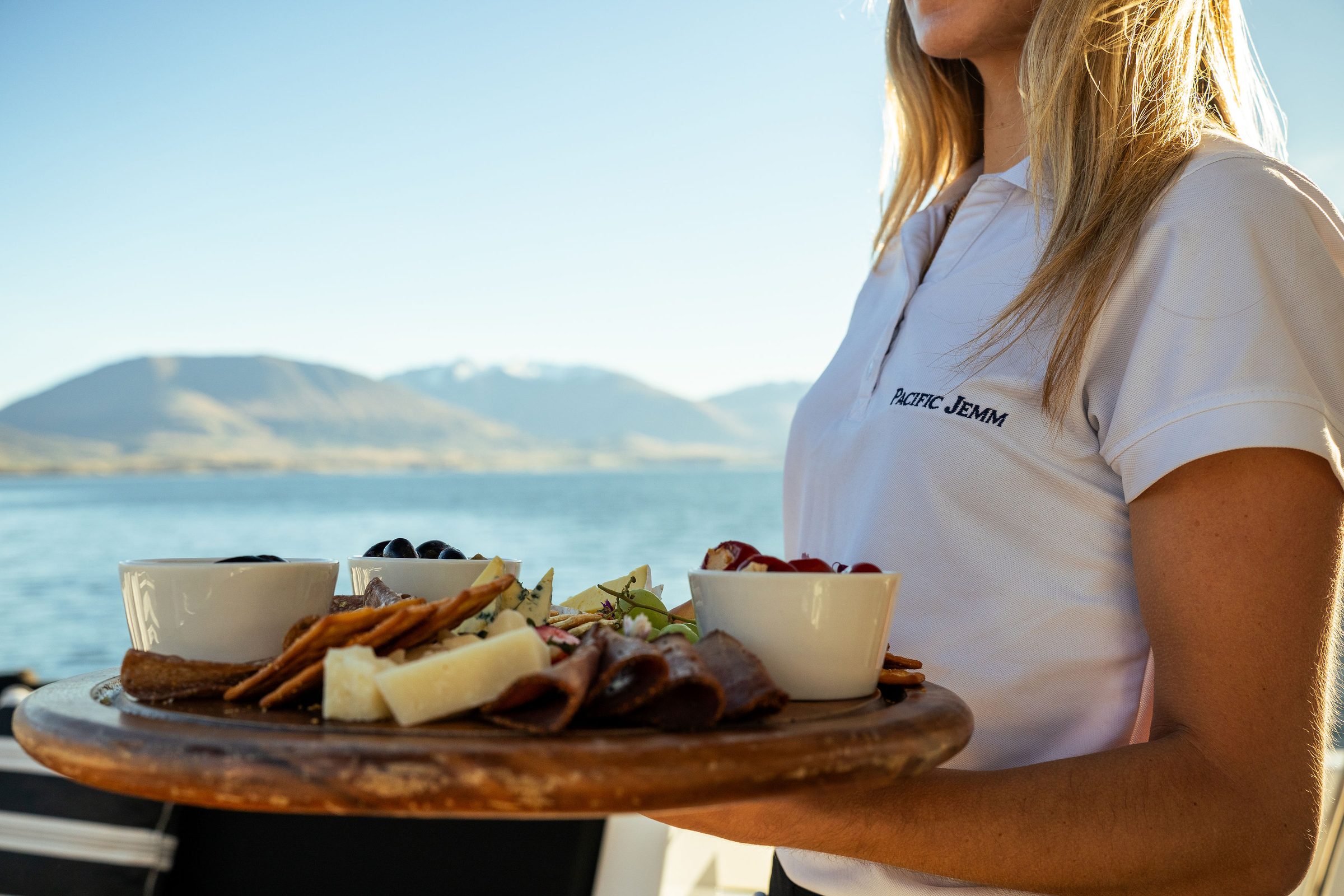 Pacific Jemm crew presenting a charcuterie platter with mountain backdrop